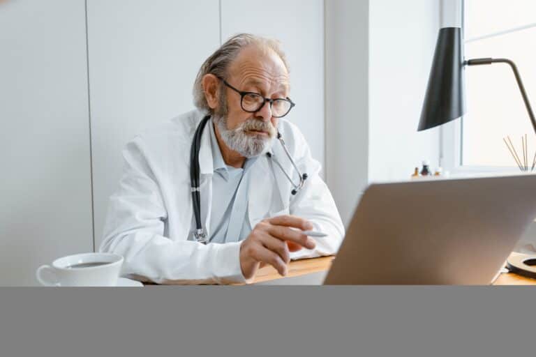 Senior doctor consulting via telehealth on laptop in clinic setting.