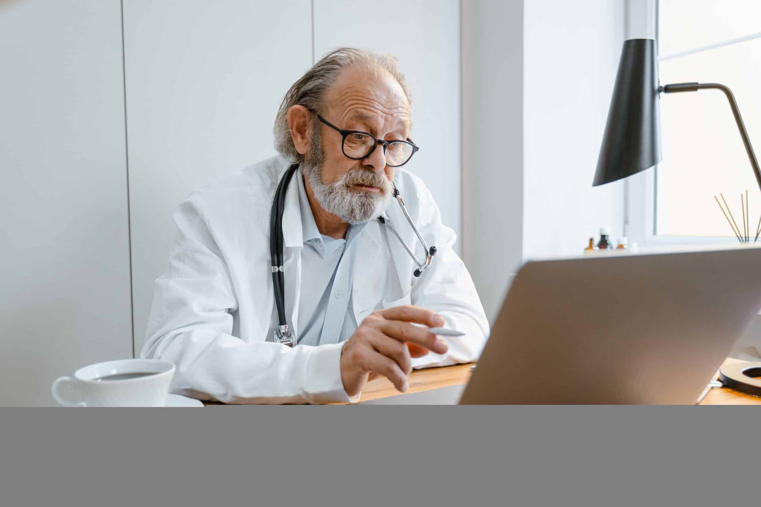 Senior doctor consulting via telehealth on laptop in clinic setting.